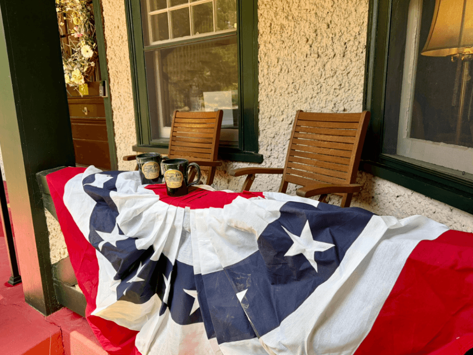 Pinecrest B&B's front porch with an American flag draped over the table and two signature Pinecrest mugs, celebrating America's 250th birthday. Pinecrest B&B's front porch with an American flag draped over the table and two signature Pinecrest mugs, celebrating America's 250th birthday.